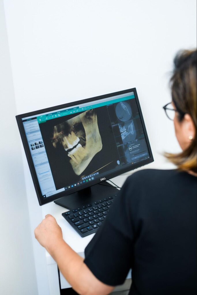 Lekarka stomatolog oglądająca trójwymiarowe zdjęcie tomograficzne szczęki pacjenta na ekranie komputera.