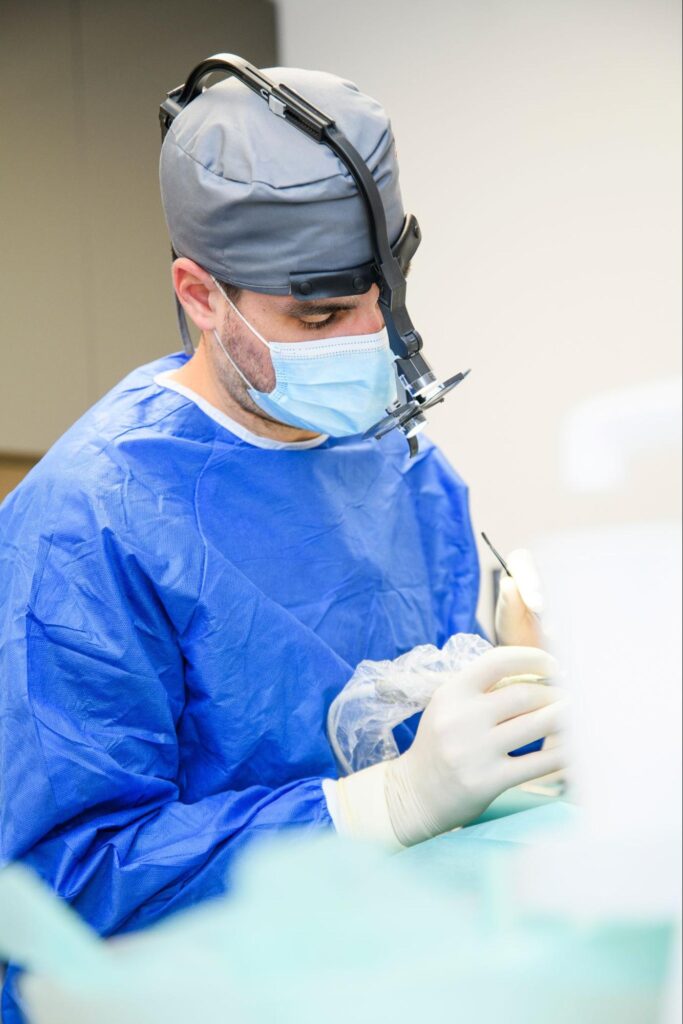 Chirurg stomatolog w maseczce i fartuchu ochronnym wykonujący zabieg.