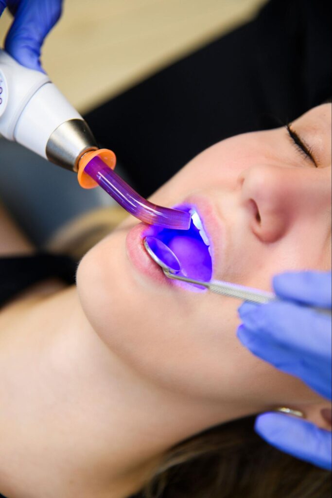 Pacjentka podczas zabiegu stomatologicznego, gdzie używana jest lampa UV do utwardzania materiału