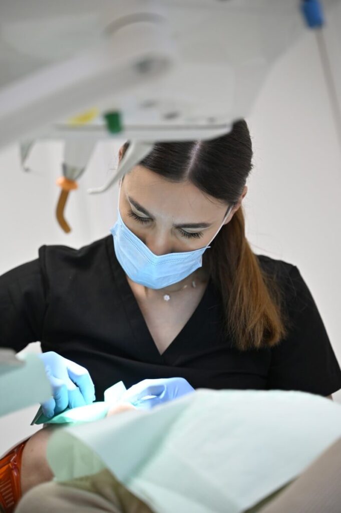 Lekarz stomatolog w maseczce ochronnej i rękawiczkach wykonujący precyzyjny zabieg dentystyczny u pacjenta.