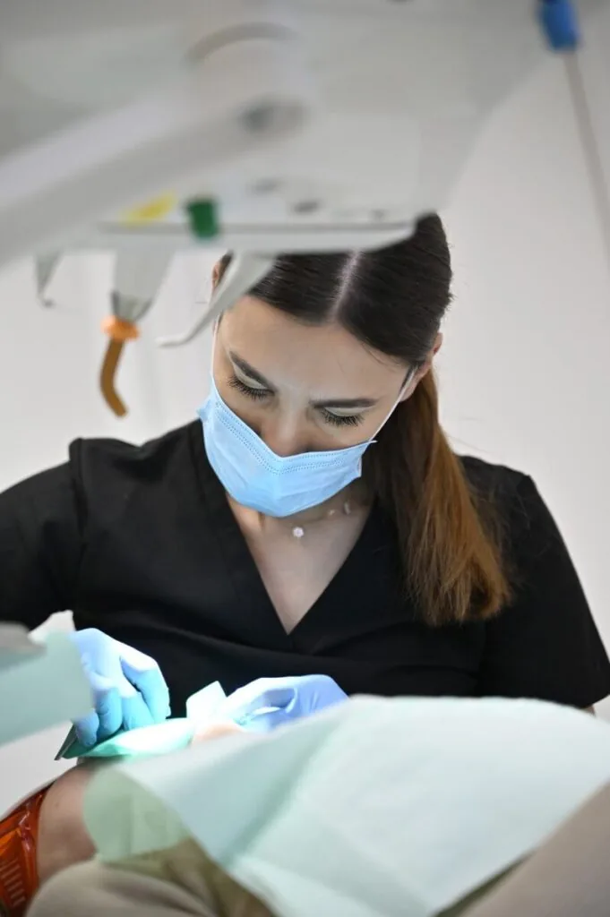 Lekarz stomatolog w maseczce ochronnej i rękawiczkach wykonujący precyzyjny zabieg dentystyczny u pacjenta.
