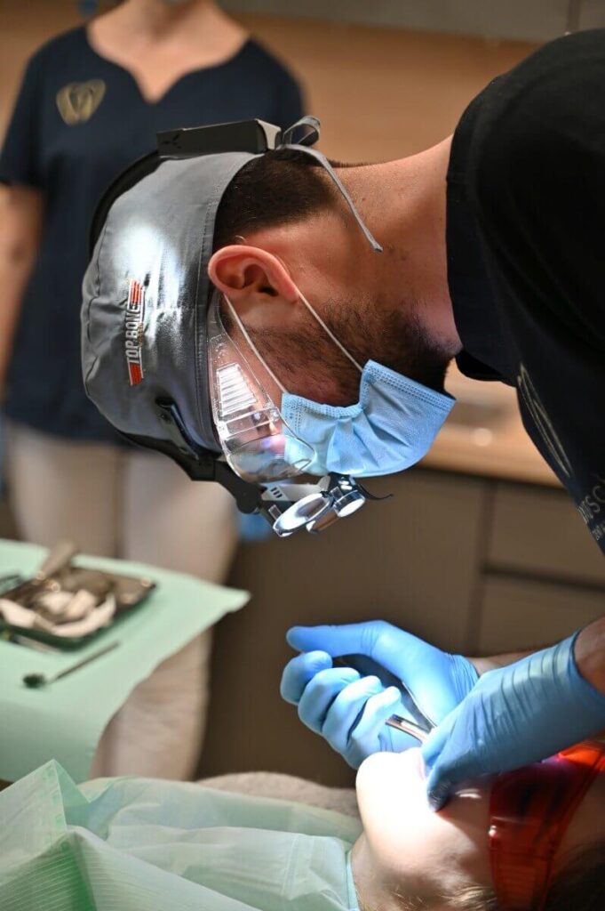 Chirurg stomatolog w lupach zabiegowych i oświetleniu czołowym wykonuje precyzyjny zabieg ekstrakcji u pacjenta.