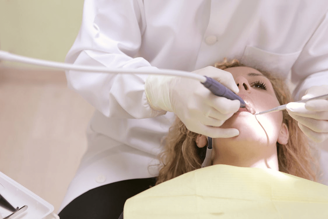 Lekarz stomatolog w białym fartuchu i rękawiczkach wykonuje precyzyjny zabieg w jamie ustnej pacjentki leżącej na fotelu dentystycznym.