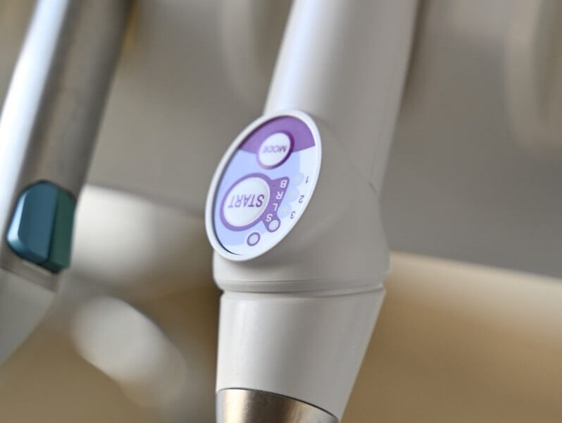 Nowoczesna bezprzewodowa lampa polimeryzacyjna z panelem sterowania, umieszczona w unicie stomatologicznym.