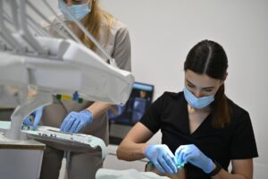 Lekarz stomatolog w czarnym uniformie i asystentka w beżowym uniformie pracują w duecie przy pacjencie; widoczne precyzyjne przygotowanie narzędzia.