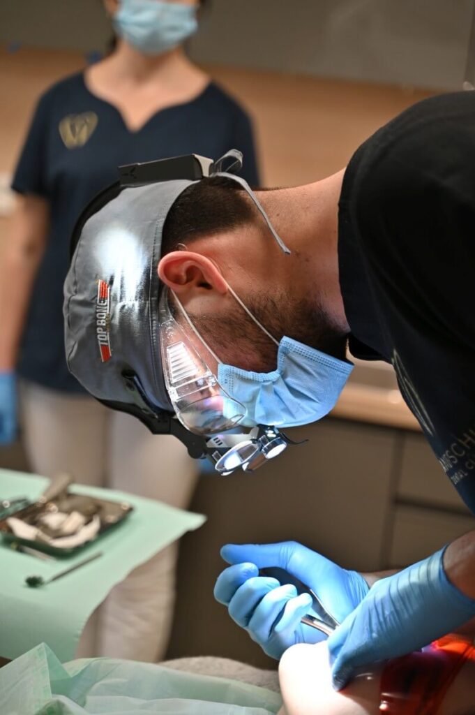 Dentysta w maskach ochronnych i lupach stomatologicznych z oświetleniem LED podczas precyzyjnego zabiegu u pacjenta.